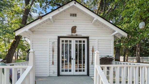 Un bâtiment en bois peint en blanc, avec une porte noire, un petit porche et une clôture en bois peinte en blanc.