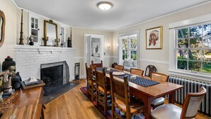 Une salle à manger avec une cheminée, une table à manger en bois, des chaises et une vue sur l’extérieur par une fenêtre.