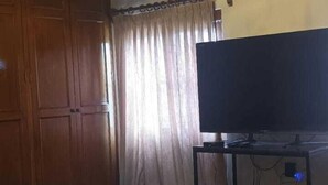 Un dormitorio con una cama grande, televisor sobre un mueble, candelabro, armario de madera y cortinas.