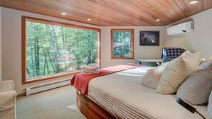Een slaapkamer met een groot raam, een bed, een stoel en een wandairconditioner.