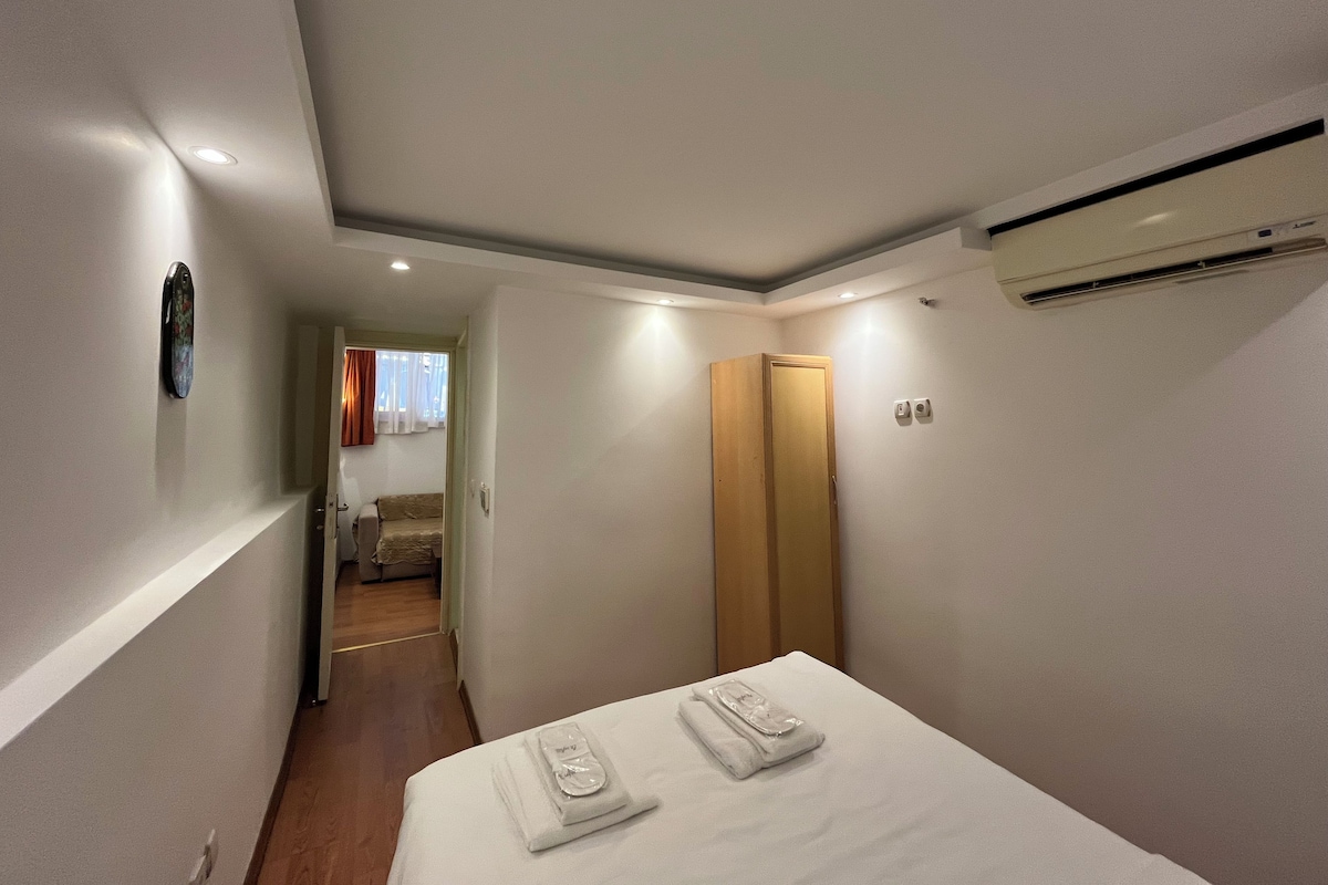 Une chambre d’hôtel comprenant un lit, une armoire en bois, un appareil de climatisation et un couloir menant à une autre pièce.