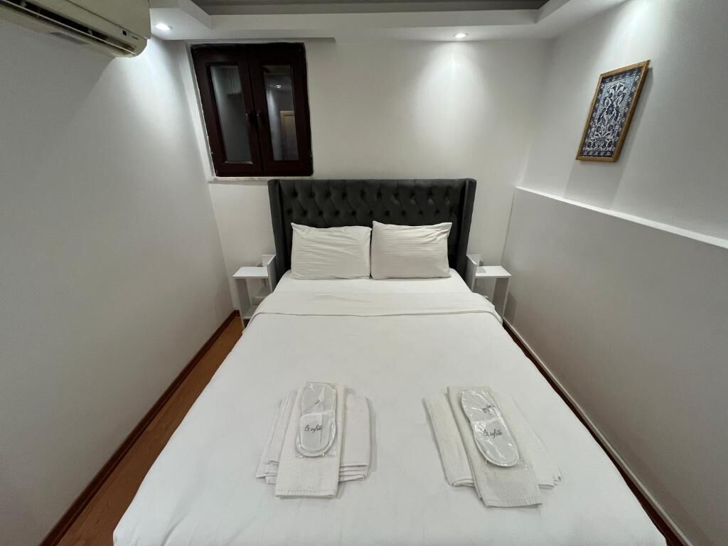 Una cama bien hecha con ropa blanca y toallas, un cabecero acolchado y una obra de arte enmarcada en la pared.