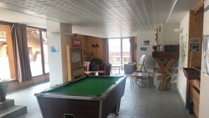 A pool table in a room with a wooden floor, a seating area with chairs, and a view through a window. - Appartement Pour 4 Personnes à 3 Minutes des Pistes Avec Salle de Détente (Orcières)