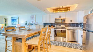 A modern kitchen with white cabinets, stainless steel appliances, and a wooden dining table.