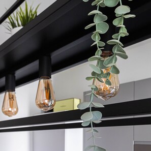 A modern kitchen with black shelves, hanging light bulbs, and a green plant. - Italianway - Lorenteggio 30 (Milan)
