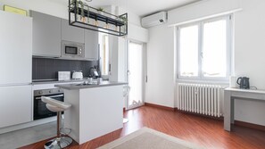 A modern kitchen with a central island, built-in oven, microwave, and a kettle on a small table. - Italianway - Lorenteggio 30 (Milan)