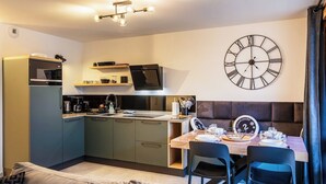 Una cucina compatta con elettrodomestici moderni, un'area pranzo con un tavolo apparecchiato per due e una grande sveglia a muro.