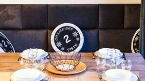 Un'area pranzo con una grande parete orologio, una testiera imbottita e un tavolo per due apparecchiato con piatti, bicchieri e posate.