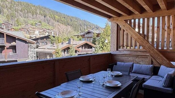 Un terrazzo in legno con tavolo e sedie, vista su una zona montuosa.