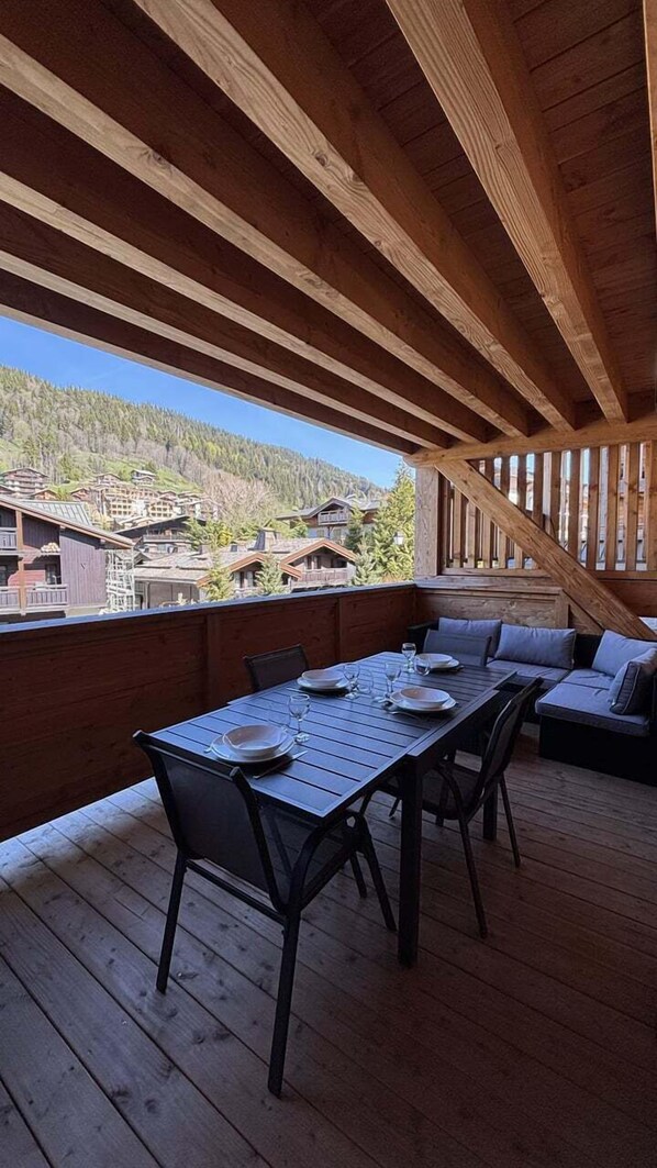 A wooden deck with a table and chairs, overlooking a mountainous area.