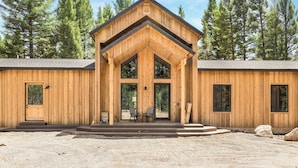Een houten lodge met een centrale ingang, grote ramen en een grindpad.