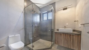 A modern bathroom with a glass-enclosed shower, a white toilet, and a wooden vanity with a sink. - Casa Lukaz Penthouse private rooftop (San José del Cabo)