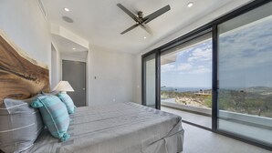 A modern bedroom with a large bed, a ceiling fan, and a view of the landscape through large windows. - Casa Lukaz Penthouse private rooftop (San José del Cabo)