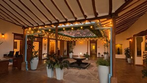 Een overdekt terras met stenen vloer, potplanten en lichtjes.