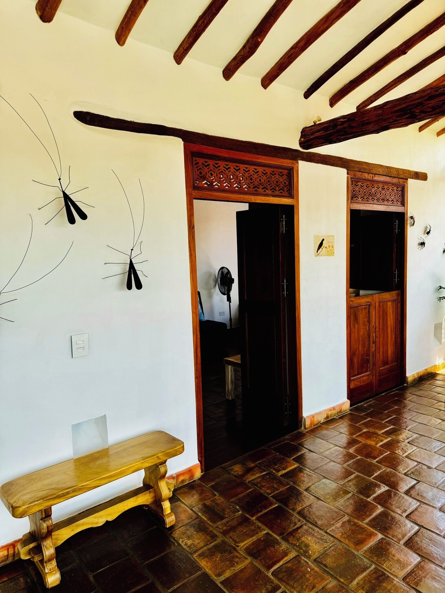 Un pasillo con un banco de madera, un ventilador y una puerta que da a otra habitación.