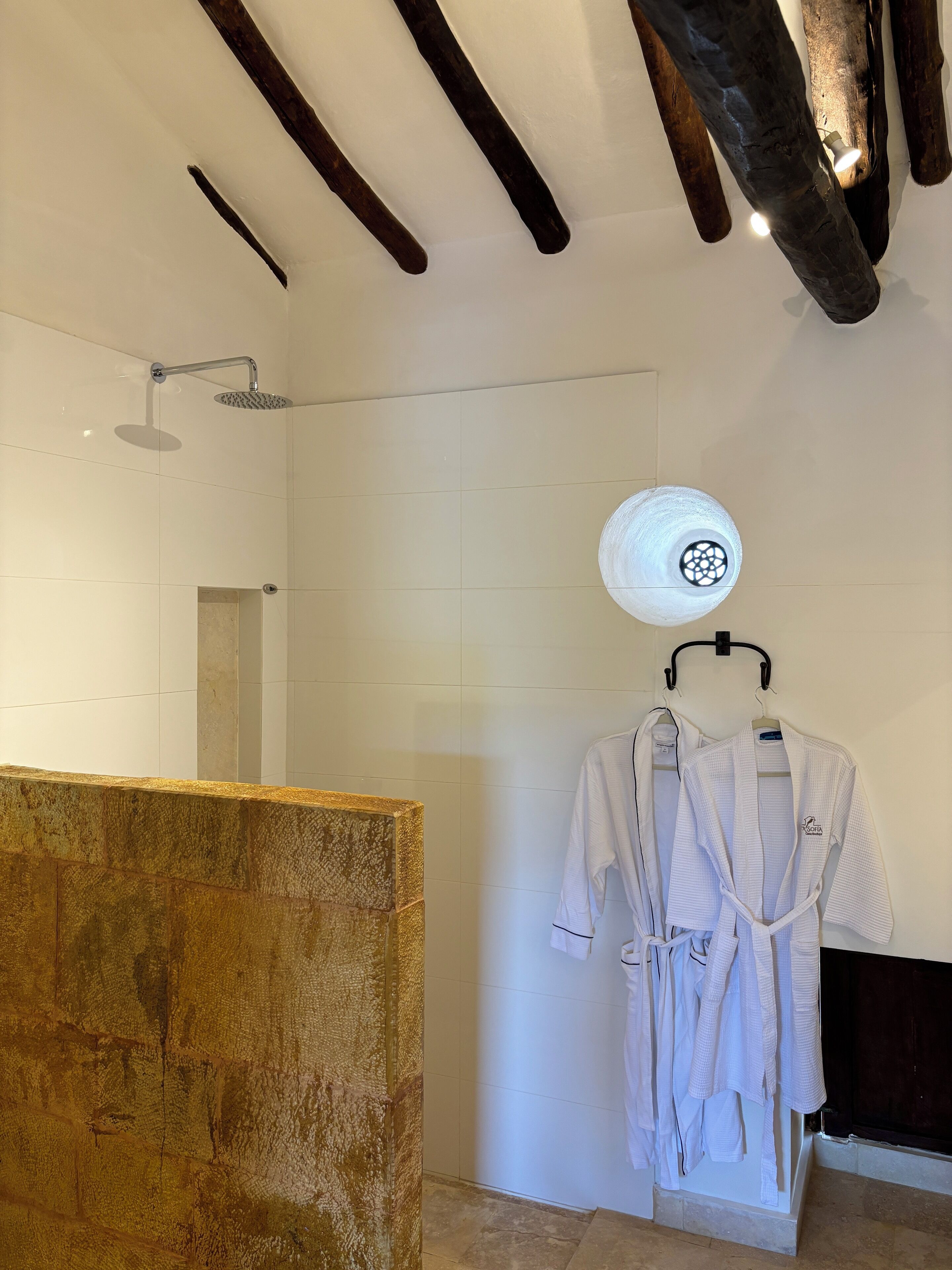 A modern bathroom with a shower, a towel rack with robes, and a textured wall.