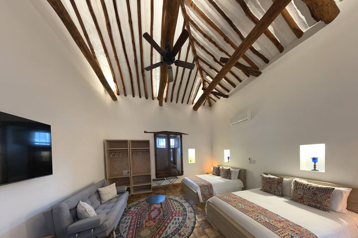 Une chambre avec un grand lit, deux petits lits, un canapé, une télévision et une armoire.