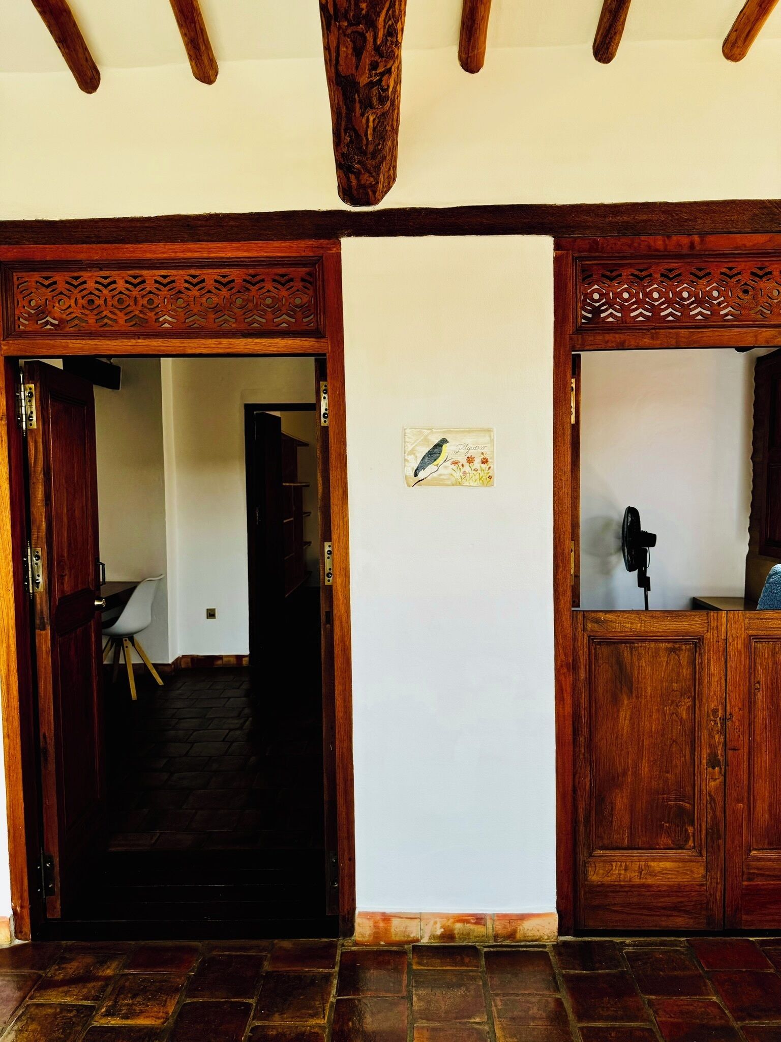 A wooden door with intricate carvings, a white wall with a bird illustration, and a stone-tiled floor.