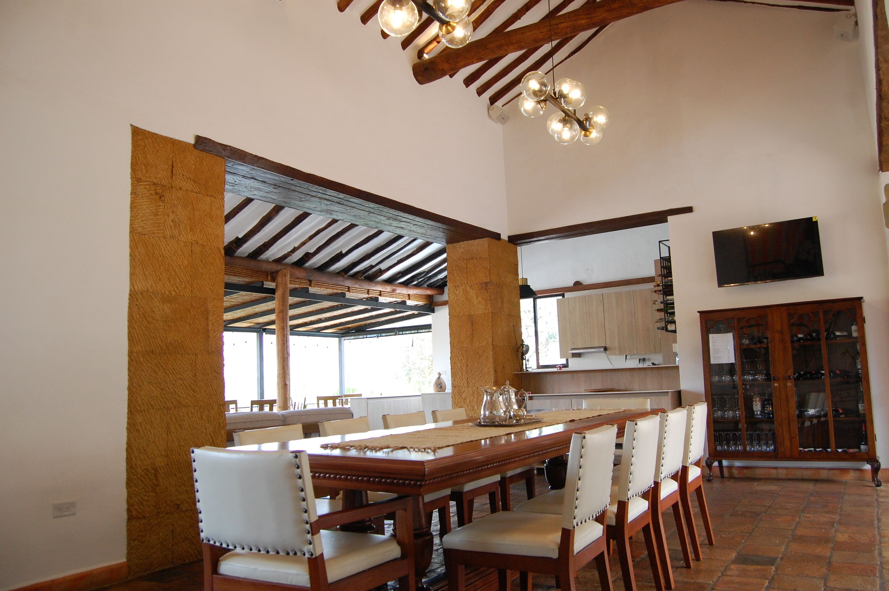 A dining area with a long wooden table, white upholstered chairs, and a chandelier.