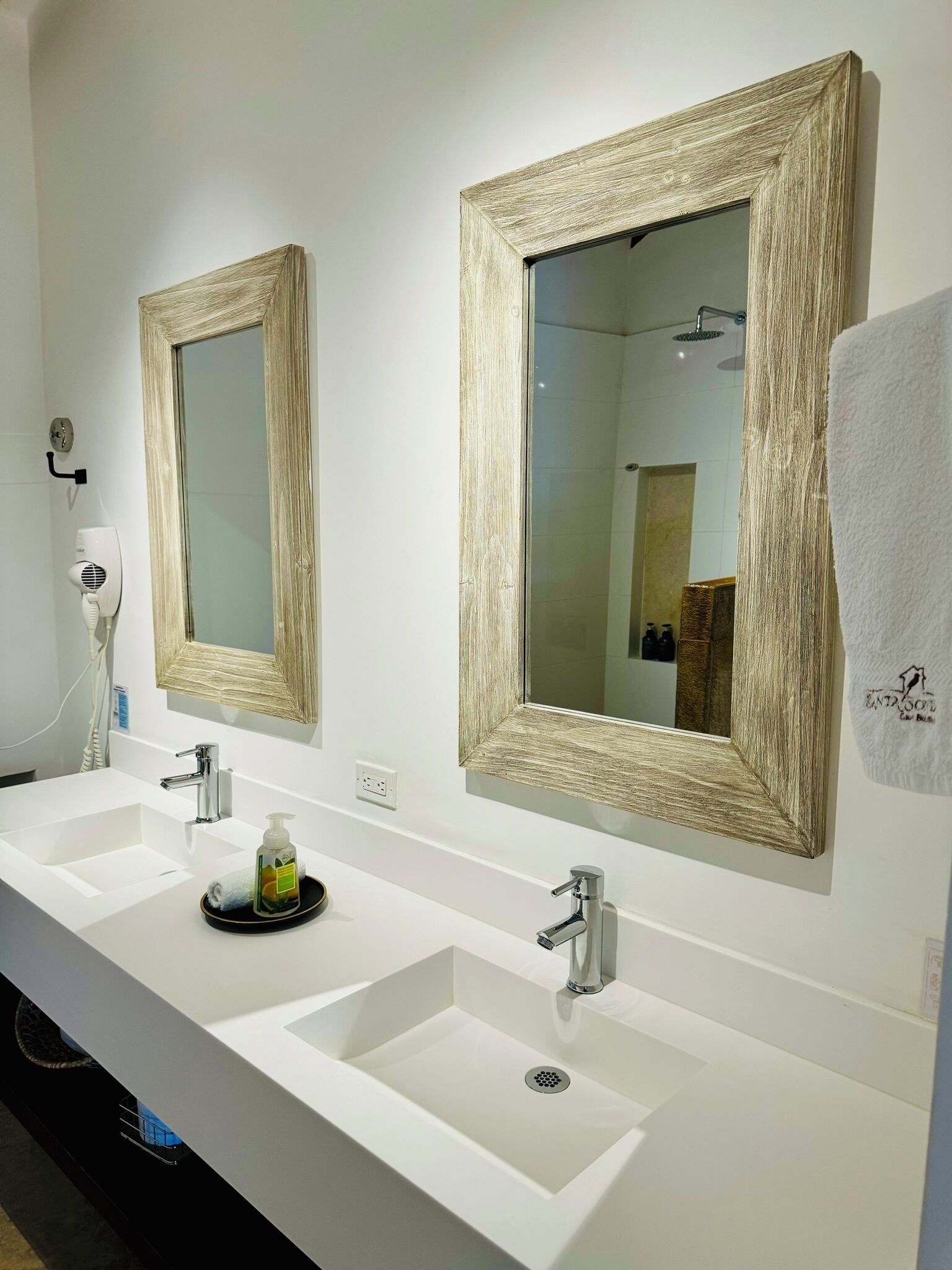 A bathroom with two sinks, a towel hanging on the wall, and a mirror with a textured frame.