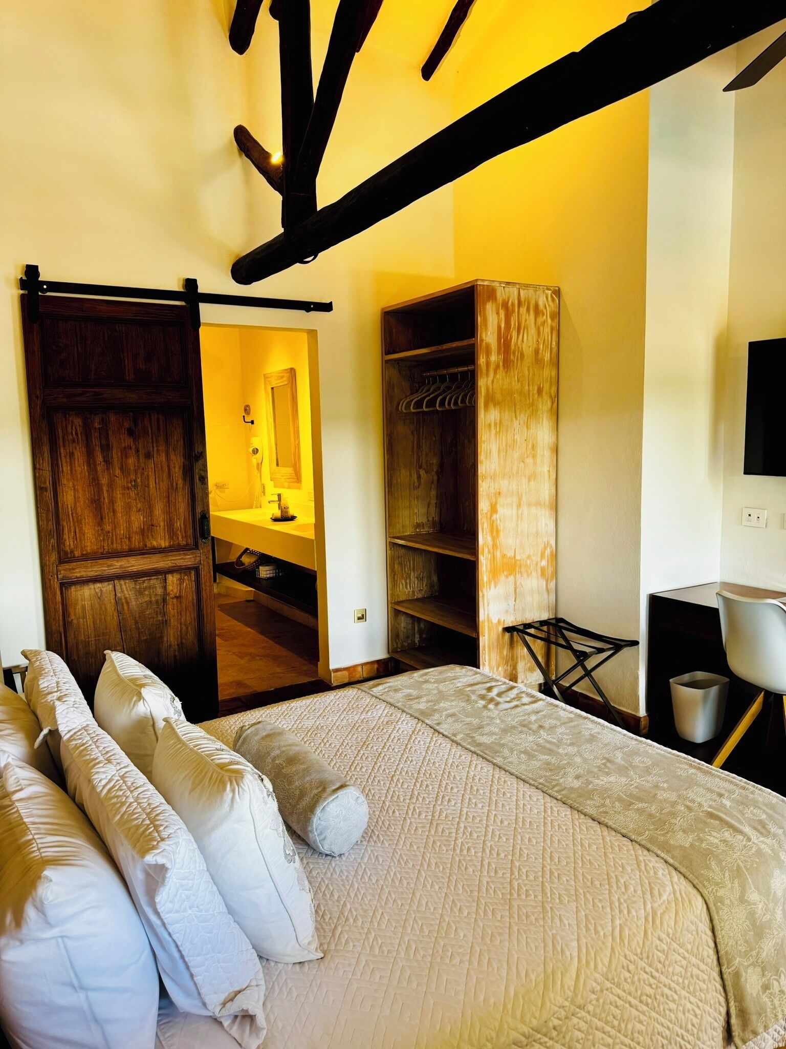 A bedroom with a large bed, a wooden wardrobe, a closet, and a TV on the wall.