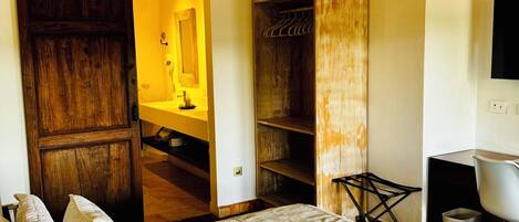 A bedroom with a large bed, a wooden wardrobe, a closet, and a TV on the wall.