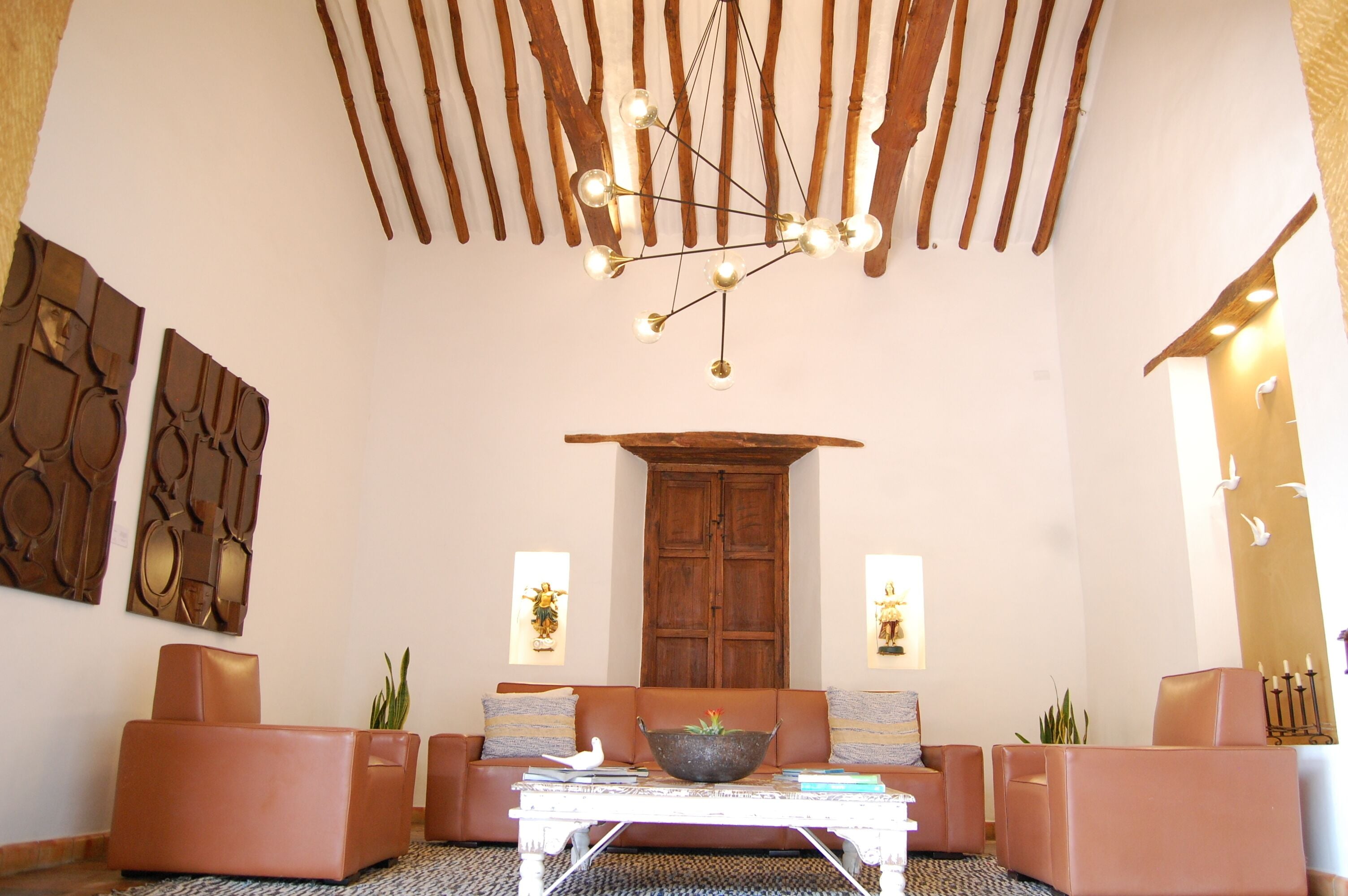 A spacious living area with a modern chandelier, leather sofas, a coffee table, and decorative wall art.