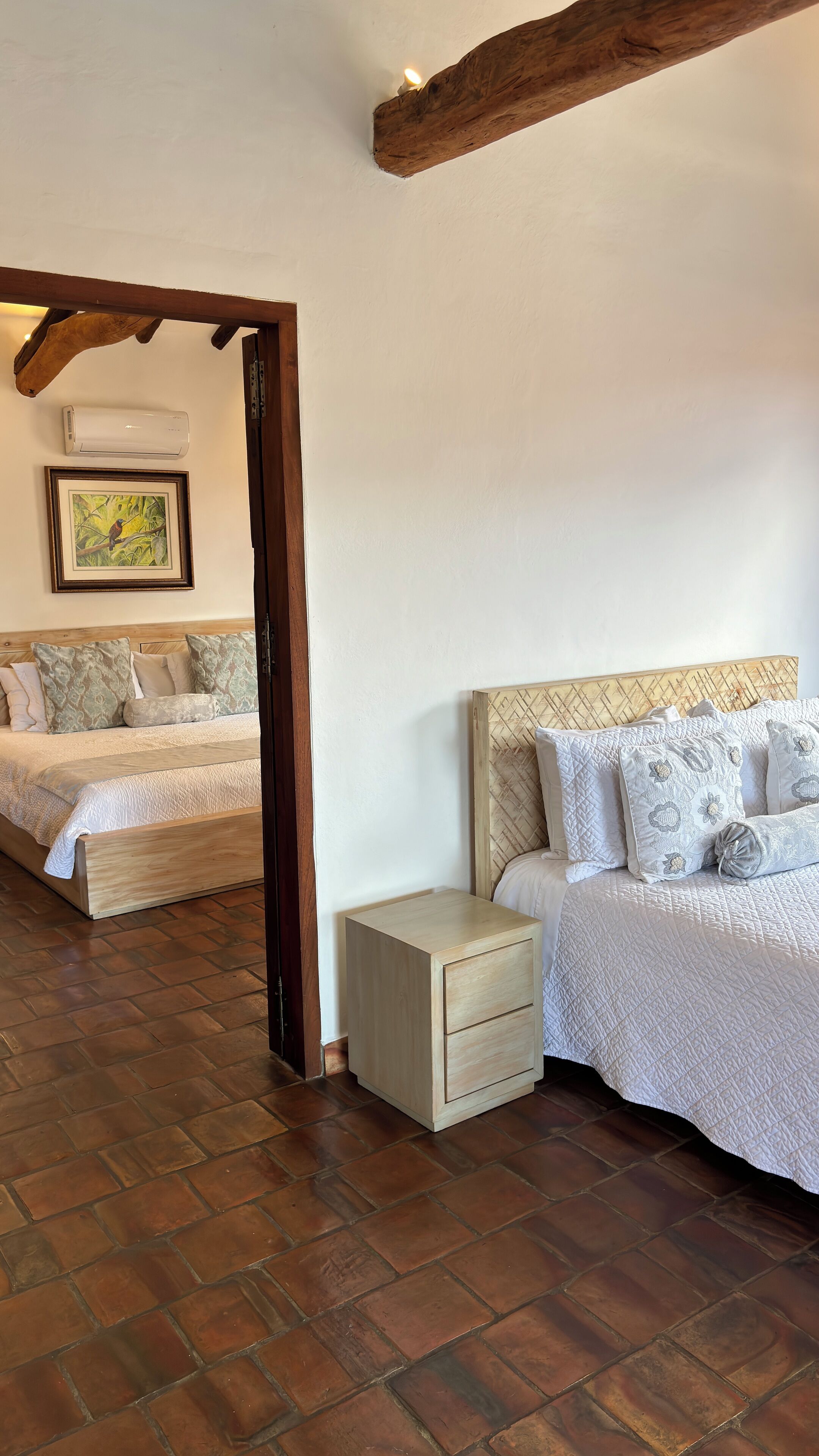 Un dormitorio con cabecera de madera, una mesita de noche, cama con ropa de cama estampada y un equipo de aire acondicionado en la pared.