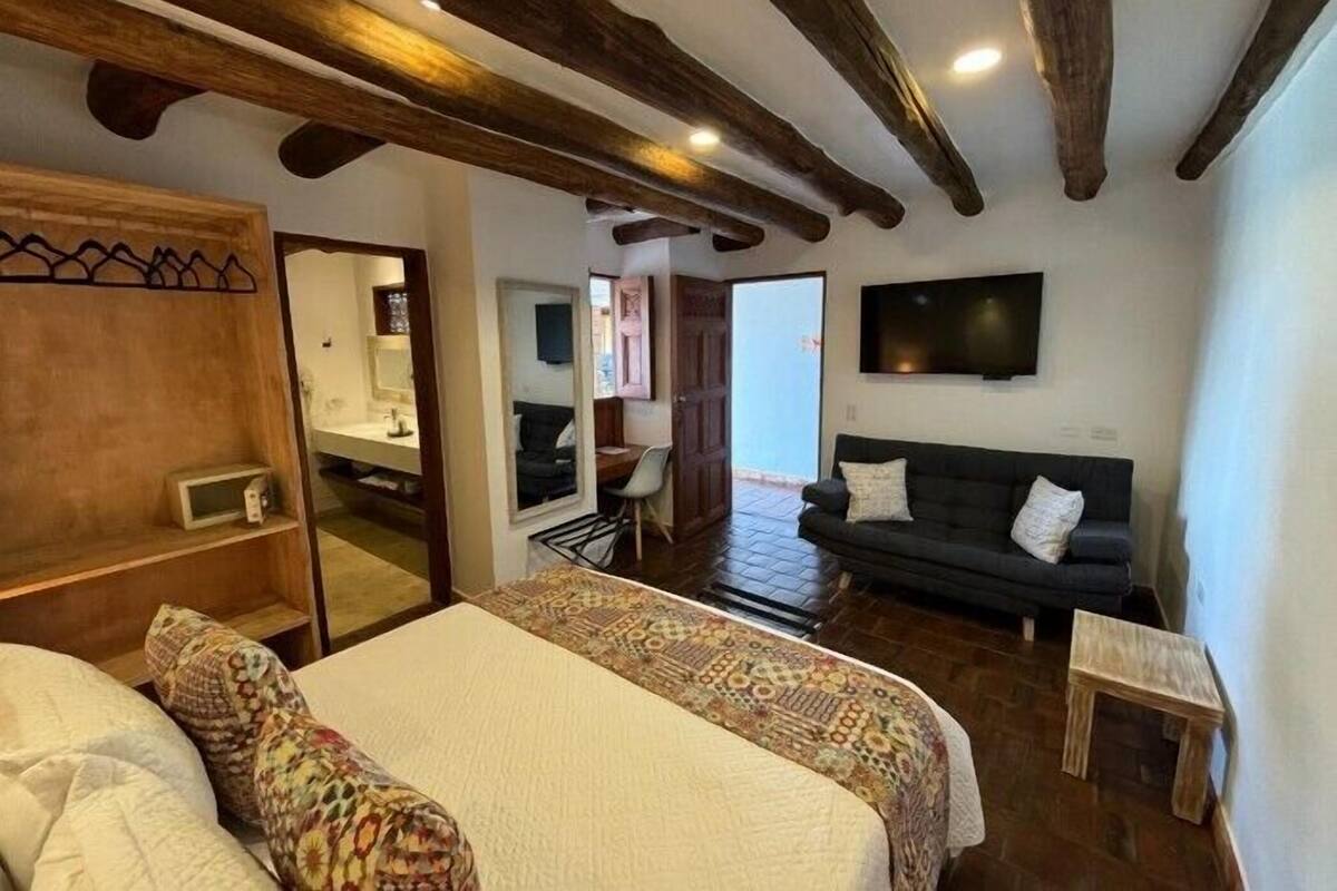 Une chambre à coucher avec un lit, un plafond en bois, un téléviseur fixé au mur et un canapé de couleur sombre.