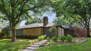 A two-story house with a brick exterior, a front yard with a stone pathway, and a small tree with red leaves.