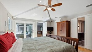 A spacious bedroom with a large bed, a ceiling fan, and a view to a balcony.