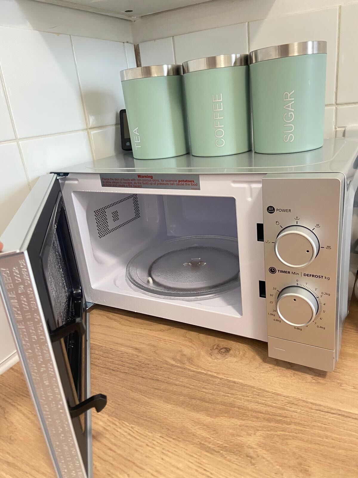 A microwave with a timer and power dial, and three containers labeled tea, coffee, and sugar on top.