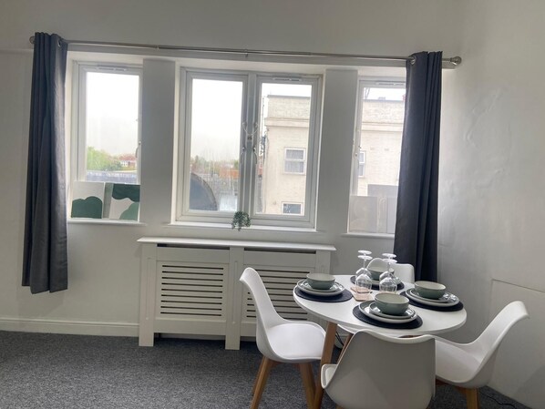 A dining area with a table set for four, white chairs, and a radiator below a window.