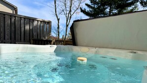 Een hottub met een drijvend object in het water, omringd door een houten terras en een witte muur.