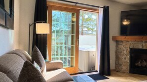 Een woonkamer met een bank, een open haard en een schuifdeur naar een hottub.