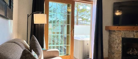 A living room with a sofa, a fireplace, and a sliding glass door leading to a hot tub.