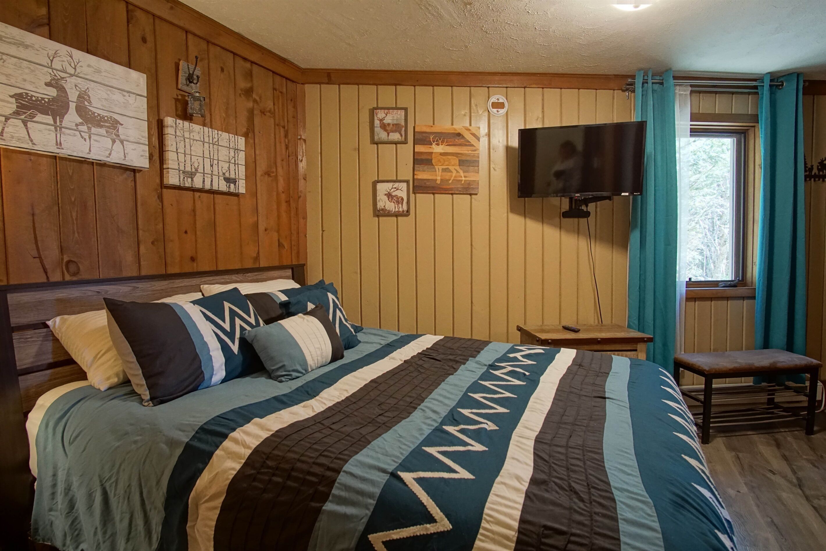 A wooden-paneled room with a bed, a television, and wall art.