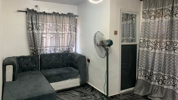 A room with a tufted sofa, a standing fan, patterned curtains, and a decorative ceiling. - Lagos - 1bed - Sleeps 2 - Aircon - Free Parking (Lagos)