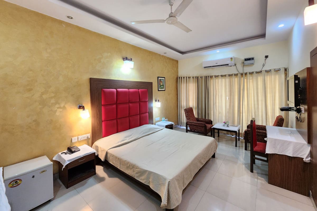 A hotel room with a bed, a desk, a chair, an air conditioning unit, and a ceiling fan.