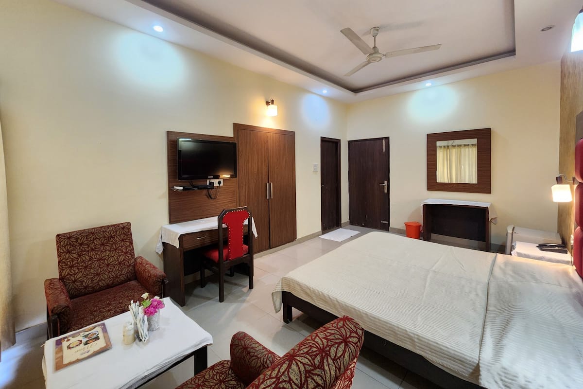 A hotel room with a bed, a desk with a chair, a TV mounted on the wall, and a ceiling fan.