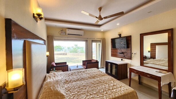 A hotel room with a bed, a desk, a chair, a TV, and a ceiling fan. - Barbet Tourist Resort (Sohna)