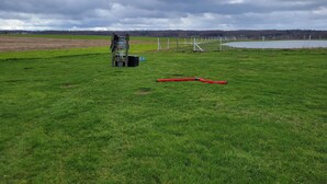 A grassy field with a white fence, a red hose, and a blue container. - Pondside Campground 2 (Meadville)
