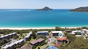 Luftaufnahme einer Küstenregion mit Strand, Gebäuden und einem Berg im Hintergrund.