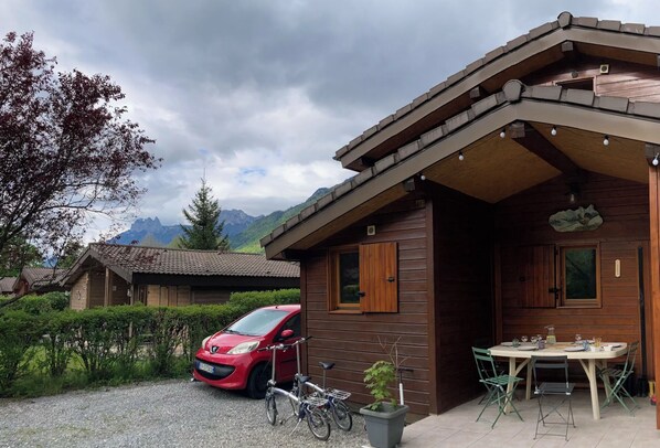 A wooden cabin with a gravel driveway, a red car, and bicycles.