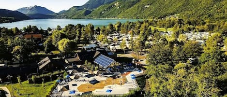 En semesteranläggning vid en sjö med flera byggnader, ett område för bad och utsikt över berg och sjön.