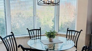 Una mesa redonda de vidrio con seis sillas, una lámpara colgante y una planta en maceta en una habitación con ventanas grandes.