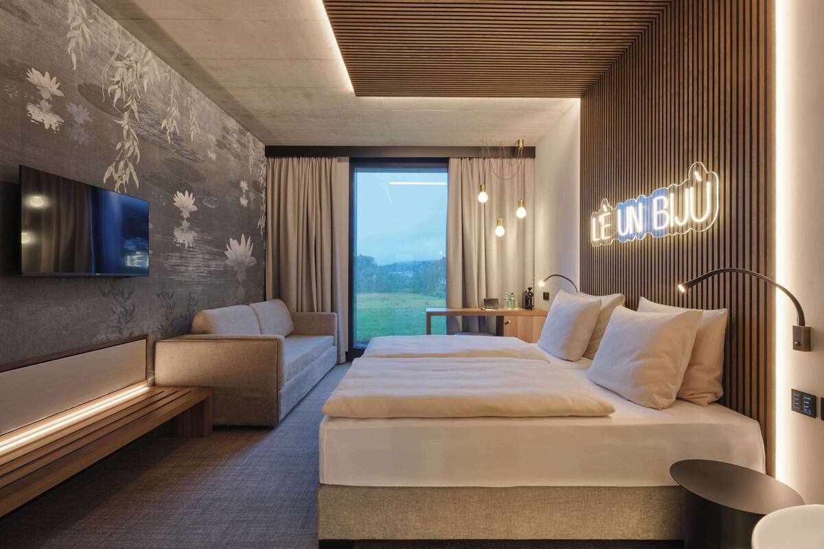 A modern hotel room with a large bed, a sofa, a desk, and a TV.