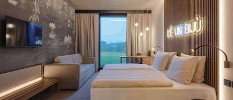 A modern hotel room with a large bed, a sofa, a desk, and a TV.