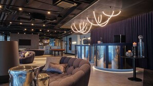 A modern lounge area with a curved reception desk, plush seating, and ambient lighting. - Dorint Resort & Spa Locarno Riazzino (Locarno)