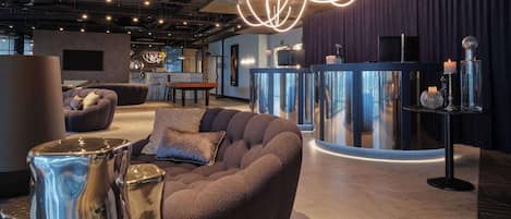 A modern lounge area with a curved reception desk, plush seating, and ambient lighting.